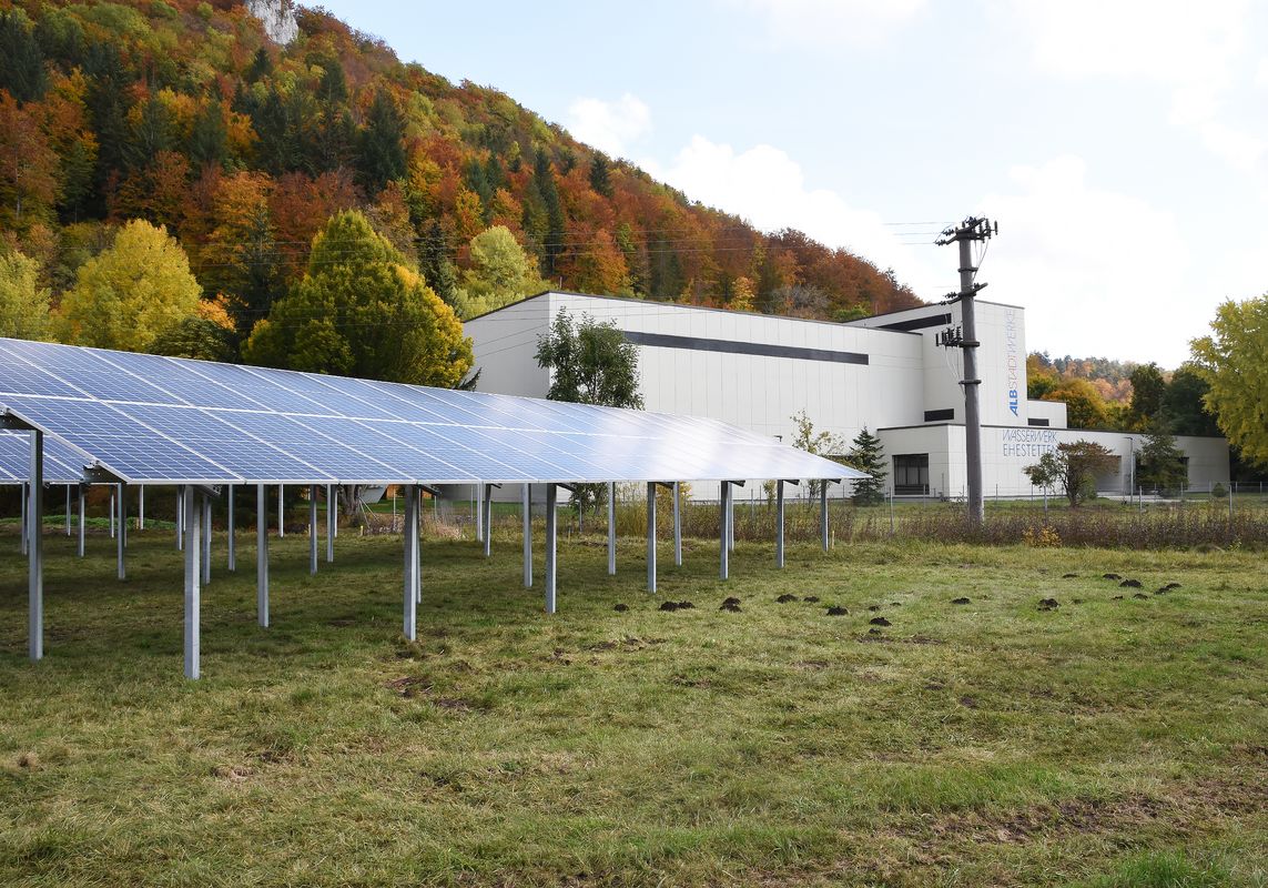Eine Wiese mit einer Photovoltaikanlage, im Hintergrund das Gebäude des Wasserwerks