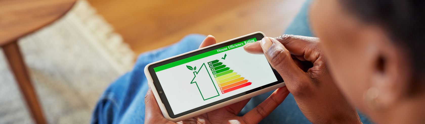 sitzende Frau mit Smartphone in der Hand auf dem ein Energiehaus zu sehen ist