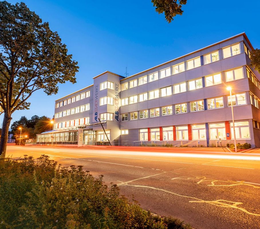 Beleuchtetes Albstadtwerke-Gebäude in der Dämmerung mit einem durchgängigen Leuchtstrahl auf der Straße